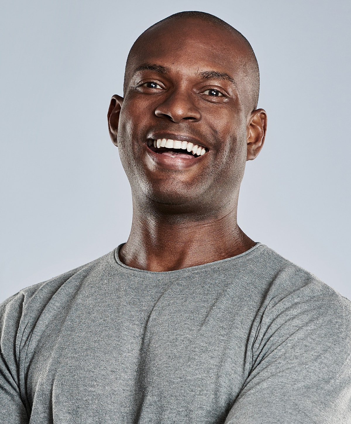Smiling man in a gray shirt against backdrop.