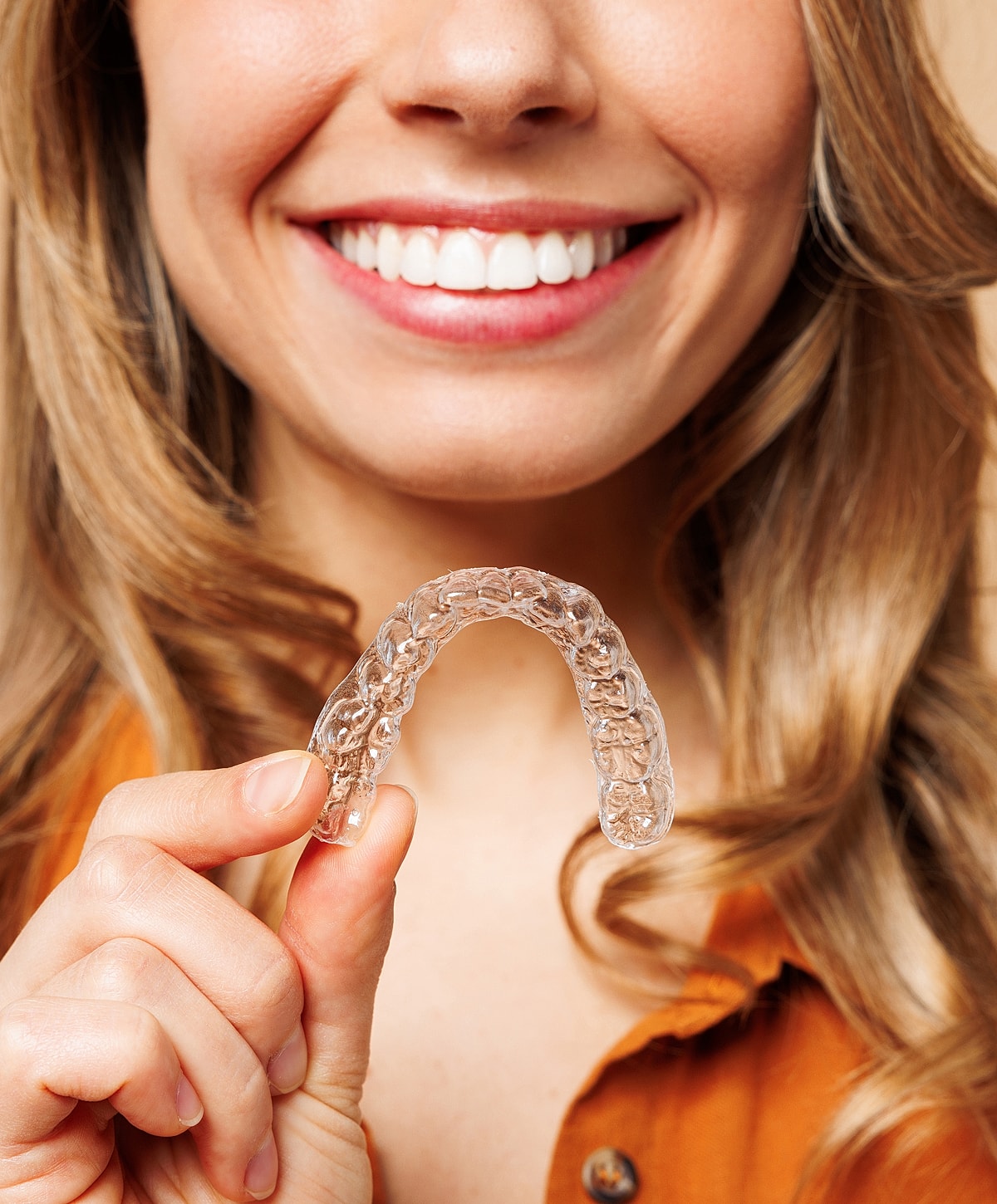 Smiling woman holding clear dental aligner.