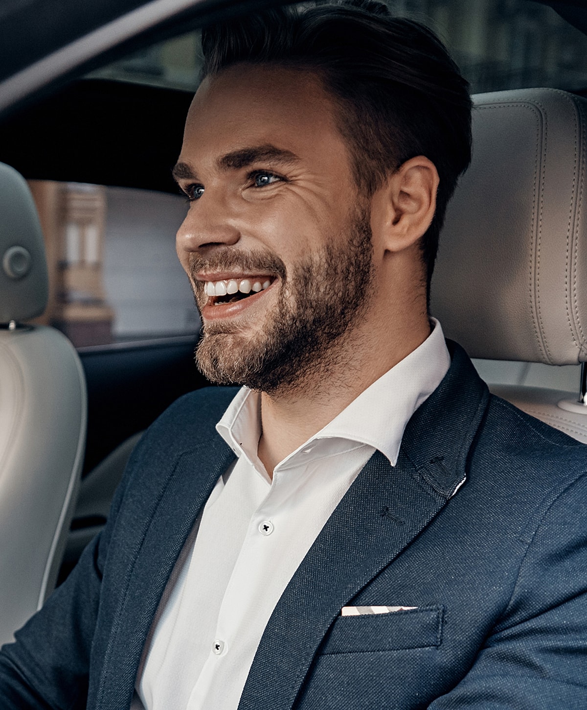 Smiling man in a car wearing a suit.