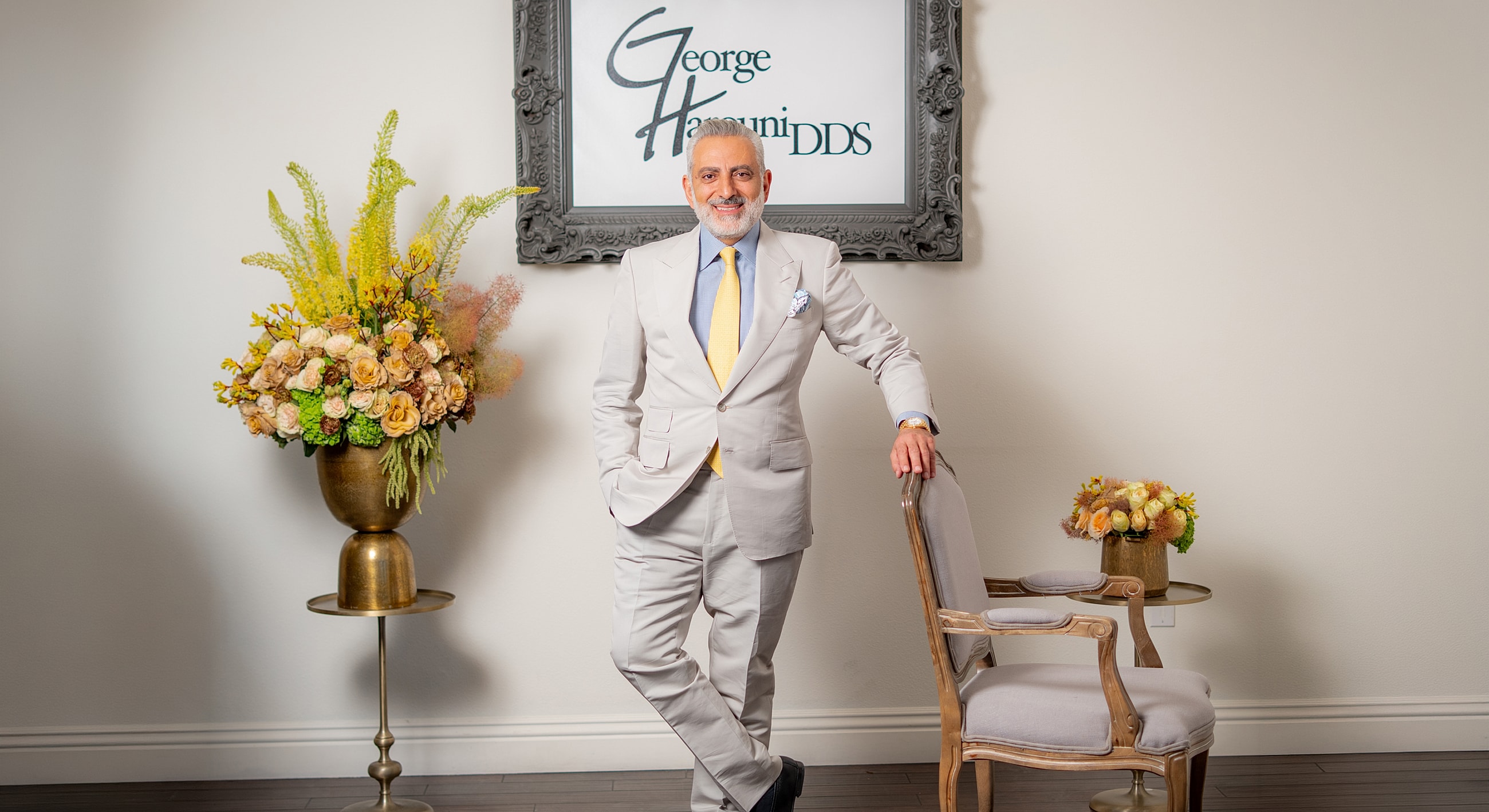 Man in suit beside floral arrangements and signage.
