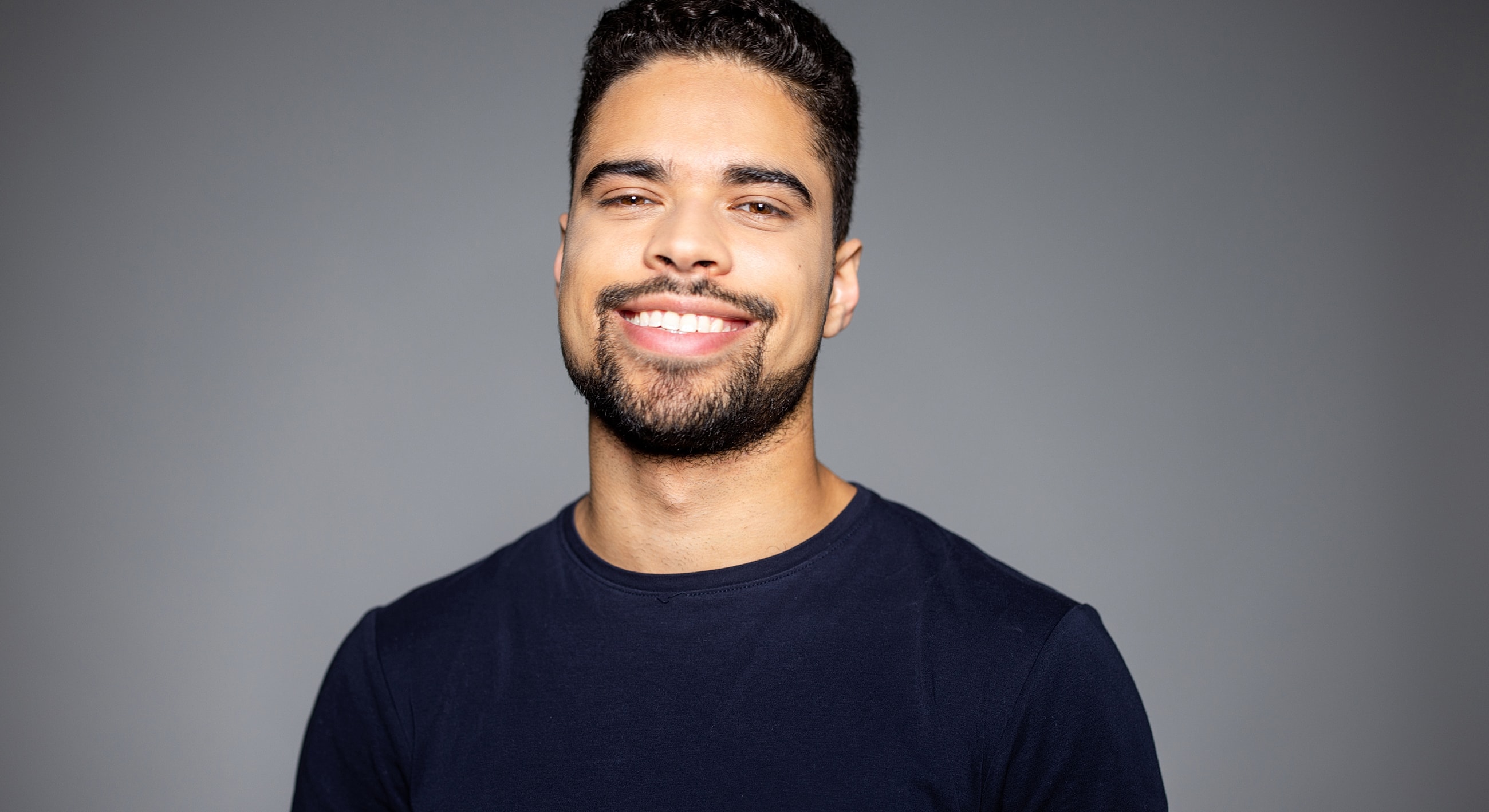 Smiling man in blue shirt against gray background.