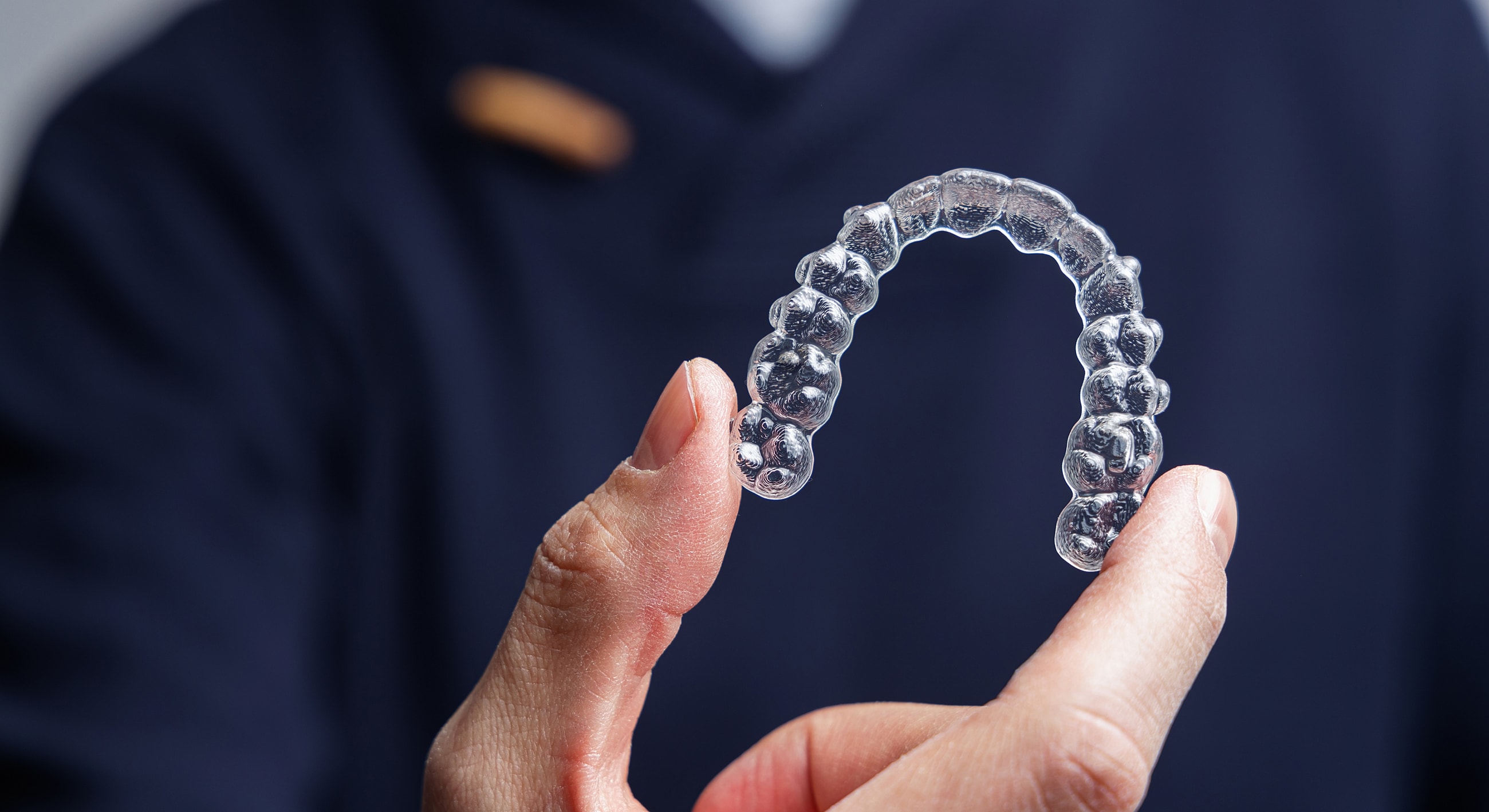 Clear orthodontic aligner held by a finger.