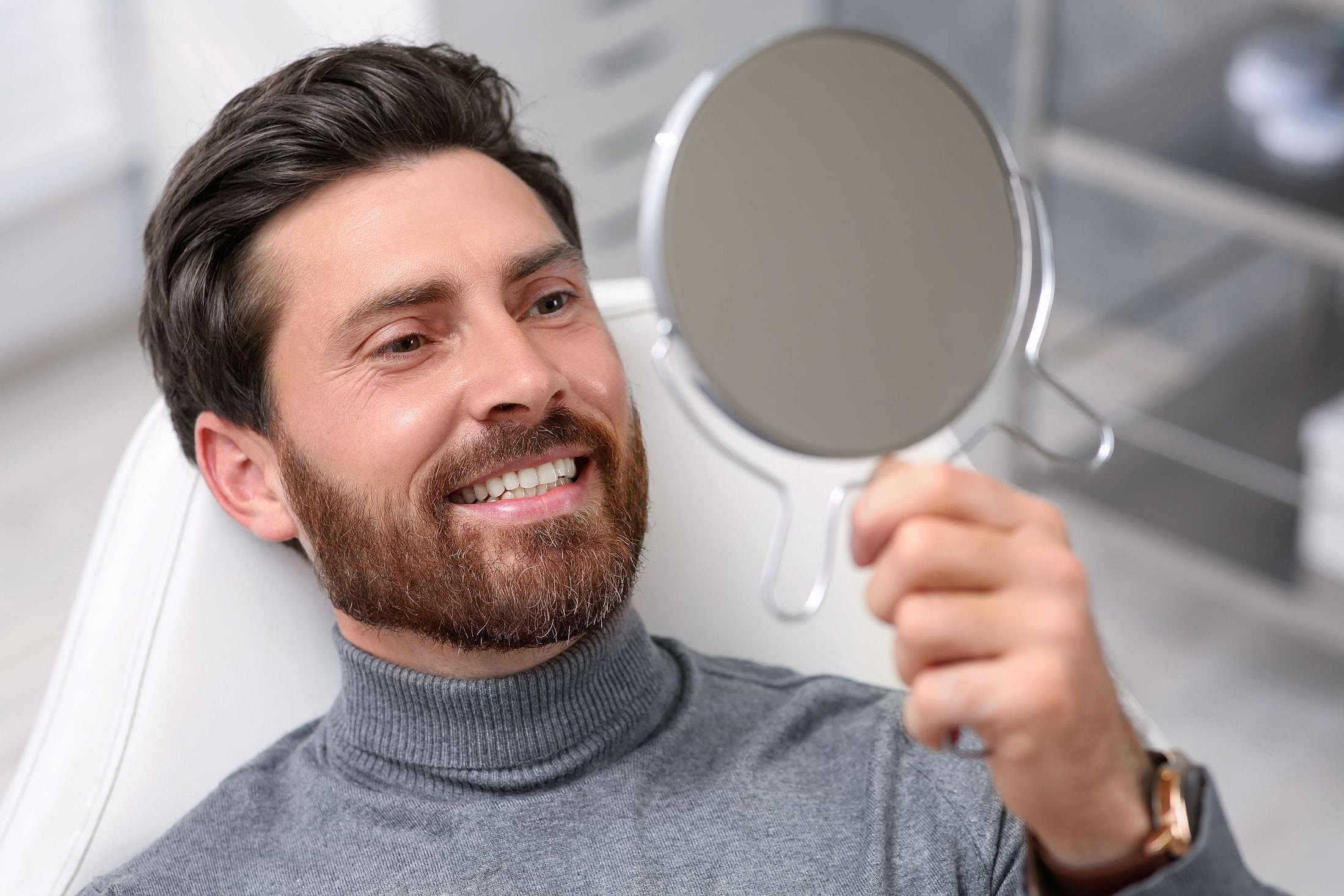 Man smiling at himself in a hand mirror.