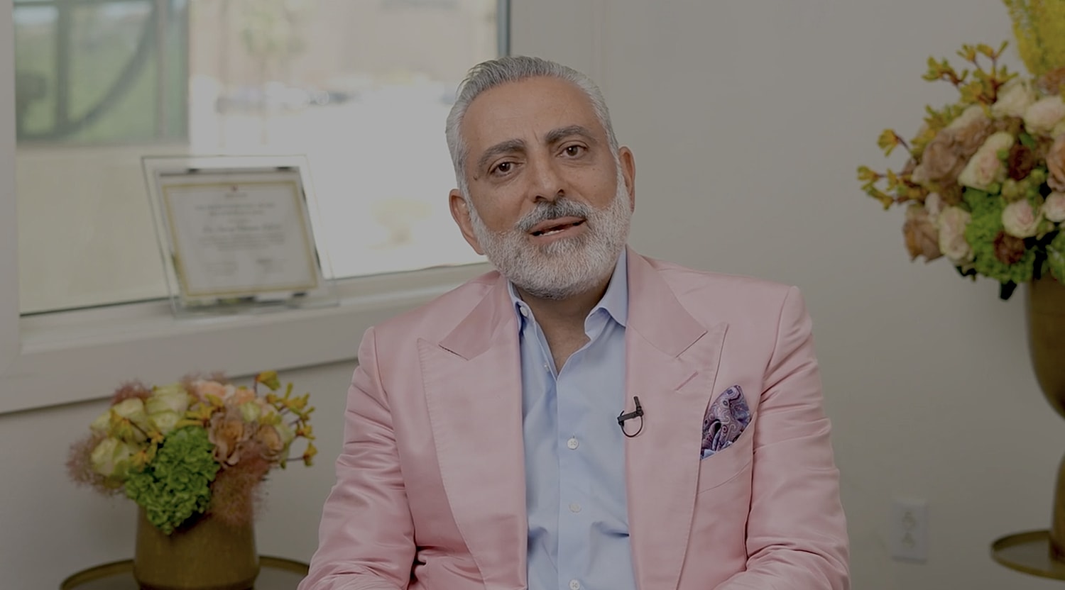 Man in pink suit speaking indoors.